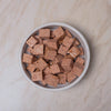Small bowl filled with cubes of Naturediet Chicken dog food on a beige surface