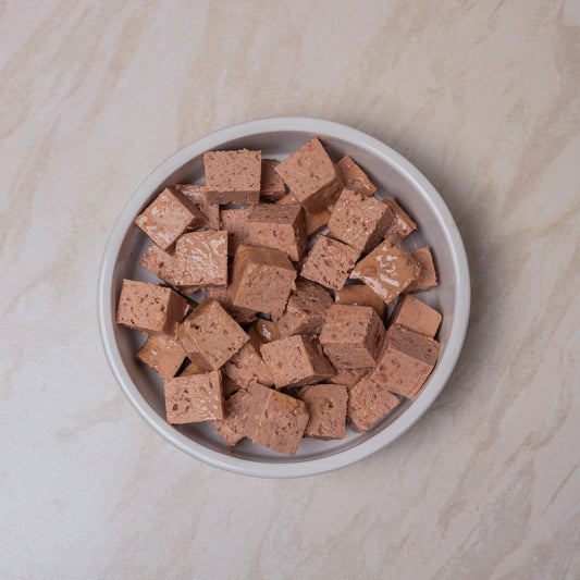 Small bowl filled with cubes of Naturediet Chicken dog food on a beige surface