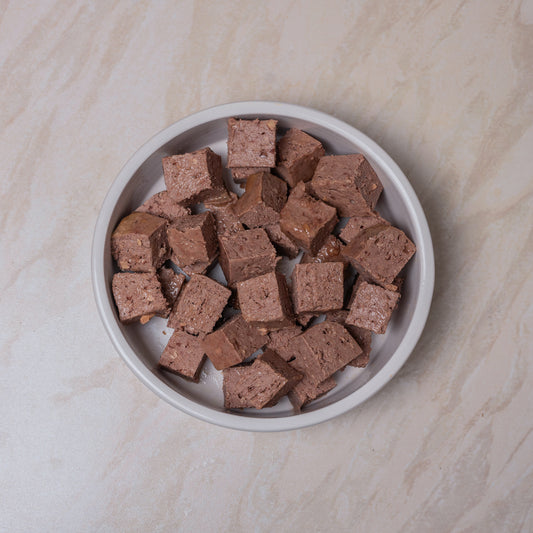 White bowl with chunks of Naturediet Lamb dog food on a beige marble background