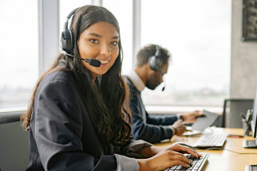 Two people working at a desk with headsets on, smiling.