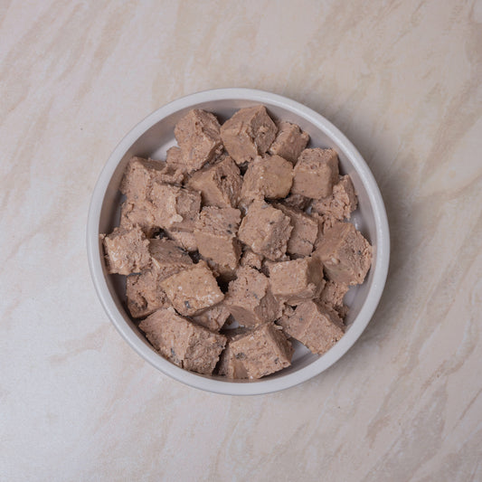 White bowl filled with chunks of Naturediet Salmon & Whitefish wet dog food on a beige surface